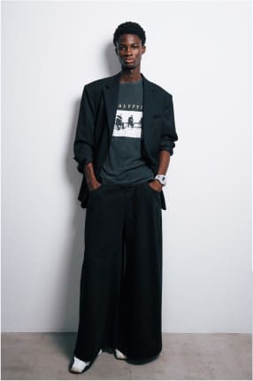 Ein Model in dunkler Kleidung posiert vor einer weißen Wand und trägt die große weiße GA-V01 Armbanduhr von G-Shock.