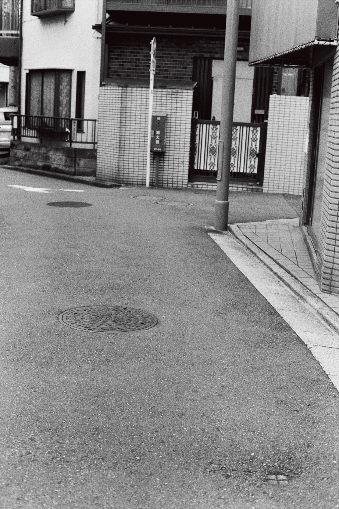 Fotografie von Yusuke Yamatani von einem Gullydeckel in einer leeren Straße.