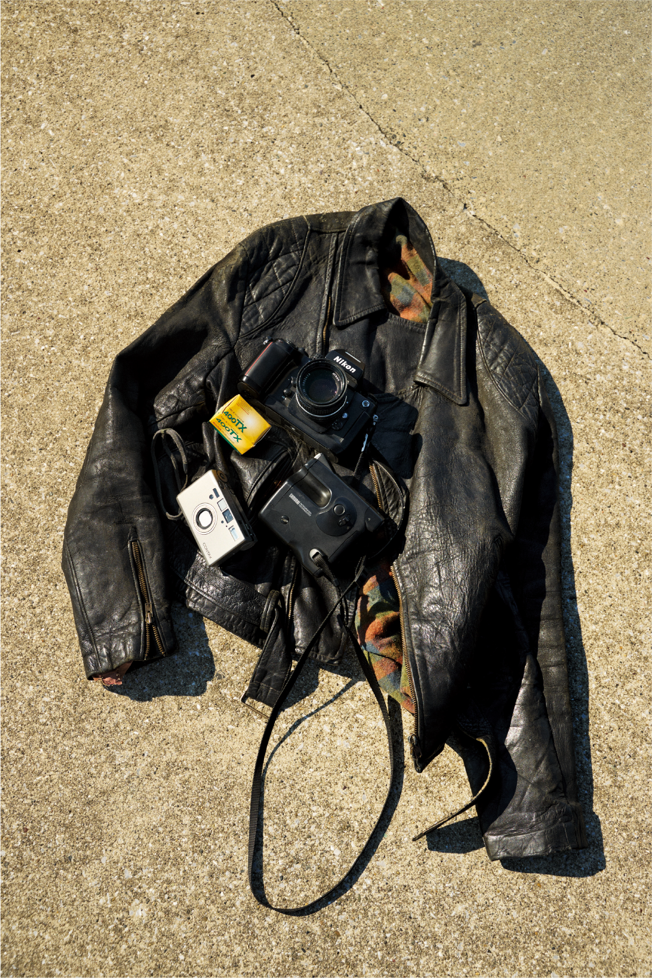 Eine schwarze Lederjacke auf dem Boden und darüber ein paar verschiedene Kameras.