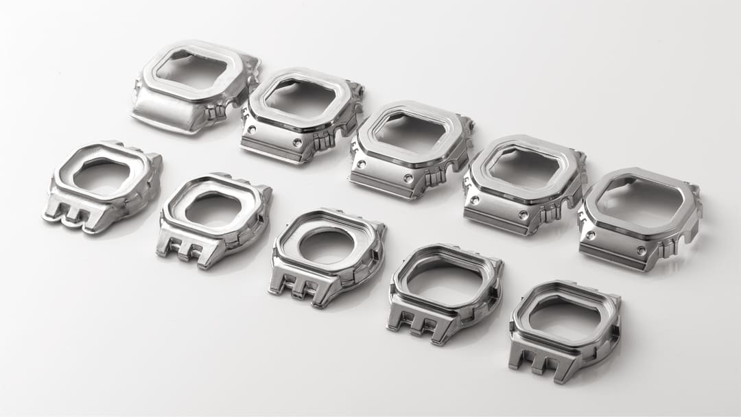 Zehn silberfarbene Lünetten in unterschiedlichen Fertigungszuständen - vom Rohling bis zur fertigen Lünette der Casio G-Shock GMW-B5000SS-2 Solaruhr