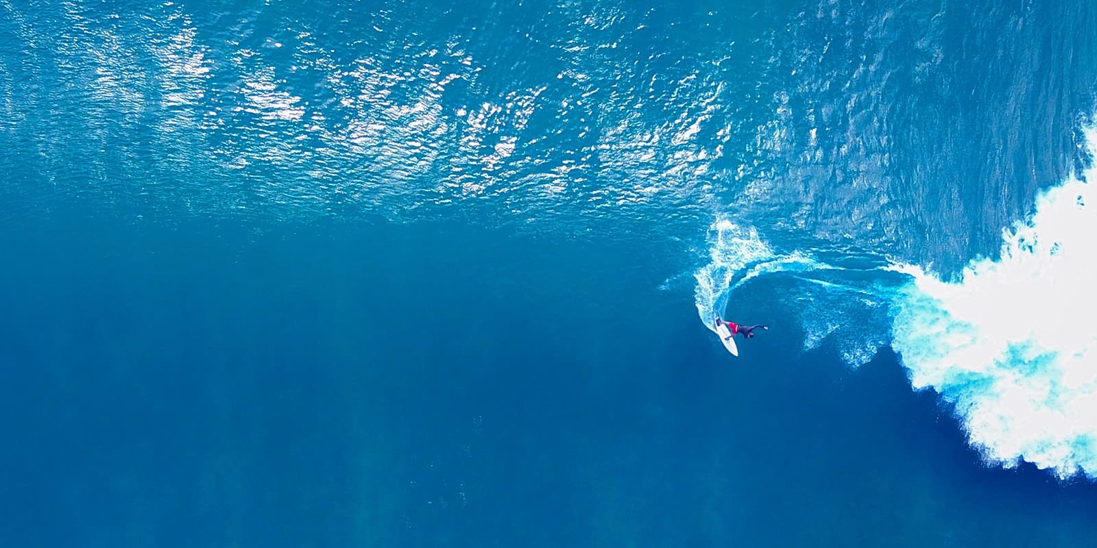 Blick von weit oben auf das Meer. Ein Surfer surft auf einer Welle.