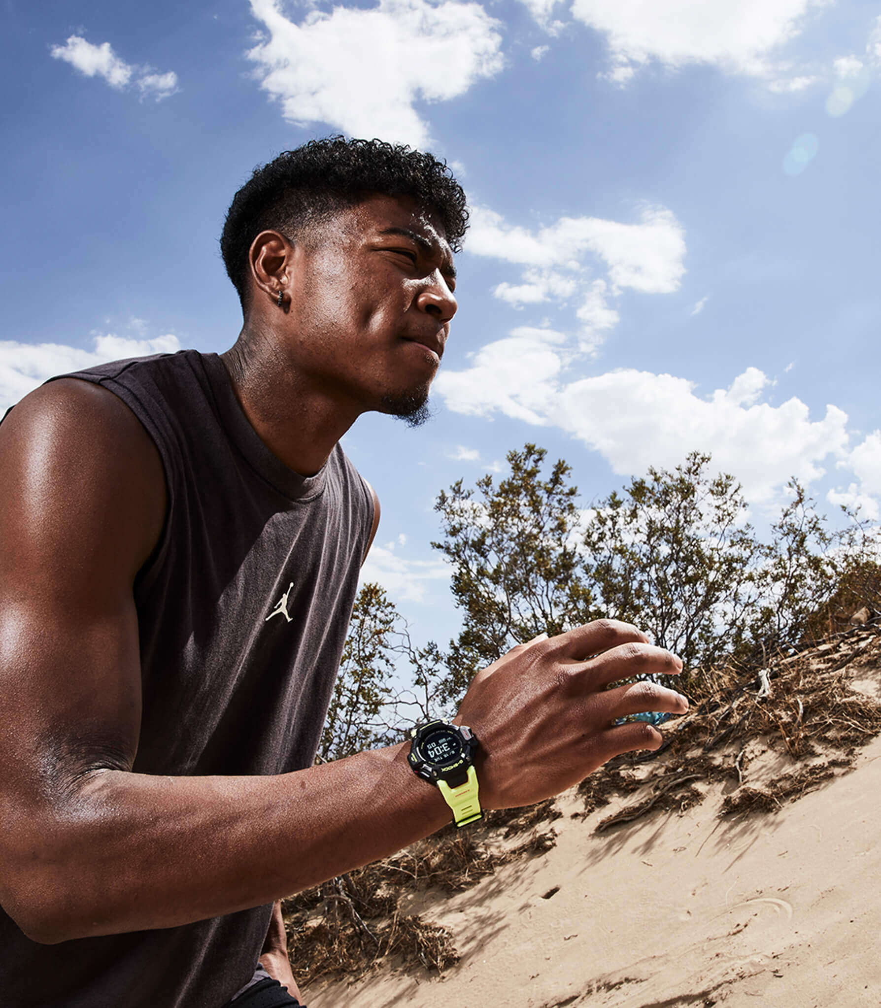 Ein Mann in einem schwarzen Shirt läuft durch eine karge Sandlandschaft, am Arm trägt er die Casio G-Squad GBD-H2000-1A9 mit gelben Armband und schwarzem Gehäuse