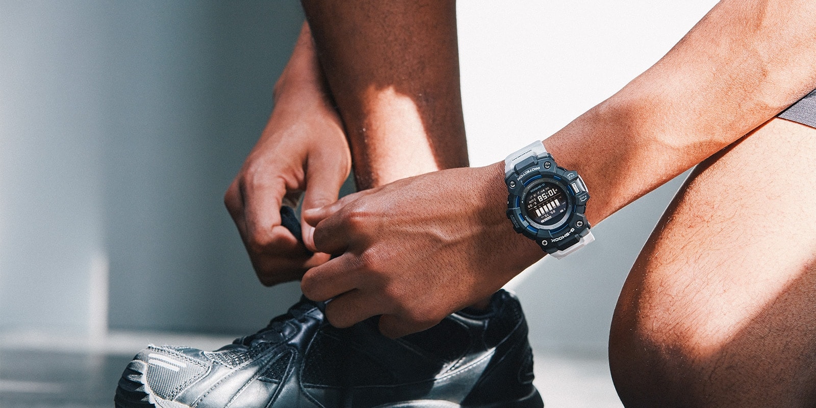Jemand bindet sich die Schnürsenkel seines Laufschuhs, am Arm trägt er die Casio G-Squad GBD-100-1A7 Armbanduhr