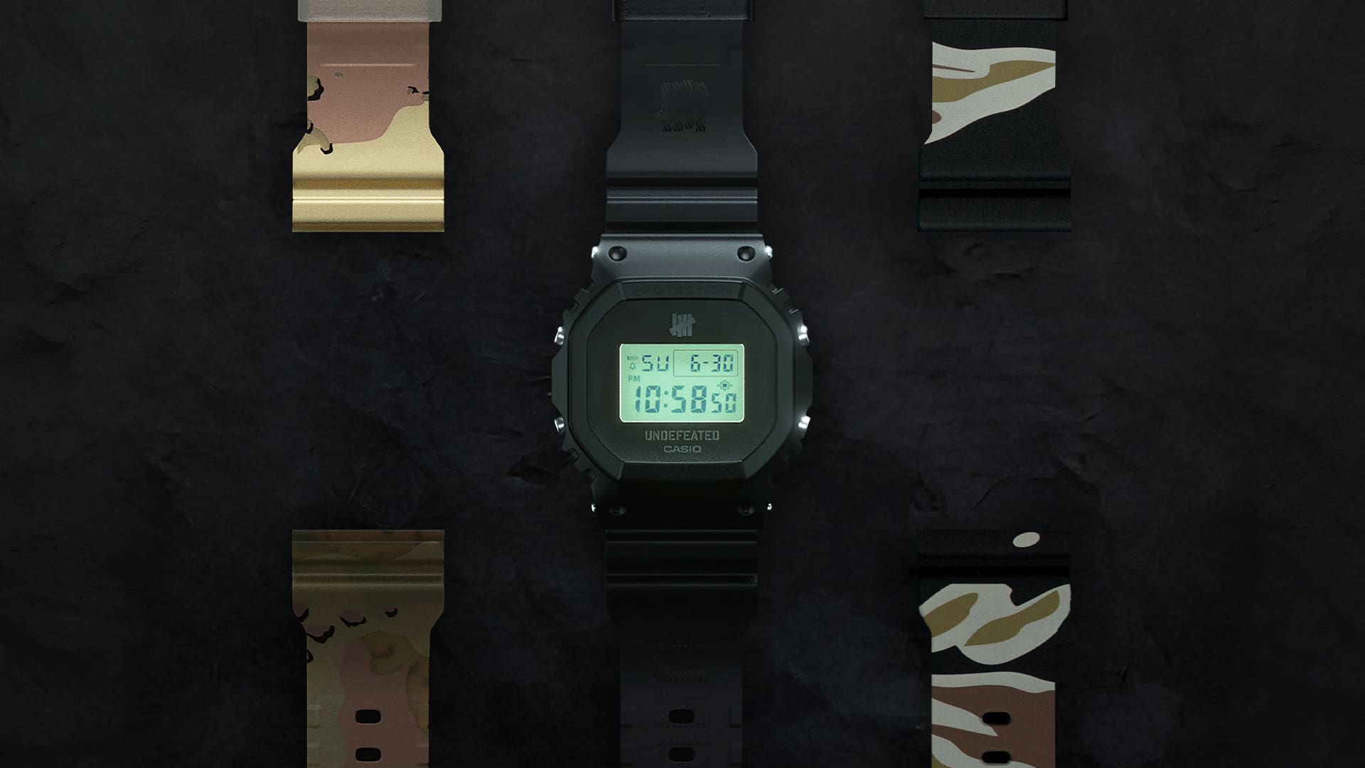 Die CASIO G-SHOCK DWE-5600UD-1 Digitaluhr mit leuchtendem LCD-Display vor einem schwarzem Hintergrund. Links neben der Armbanduhr mit ihrem transparenten, schwarzen Armband liegt das Austauscharmband im Sturm-Camouflage-Design, rechts neben ihr liegt das Austauscharmband im Tiger-Camouflage-Design