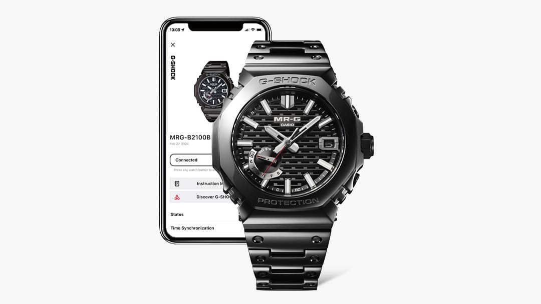 Die MRG-B2100B Armbanduhr in schwarz neben einem Smartphone, auf dem die CASIO Watches App geöffnet ist.