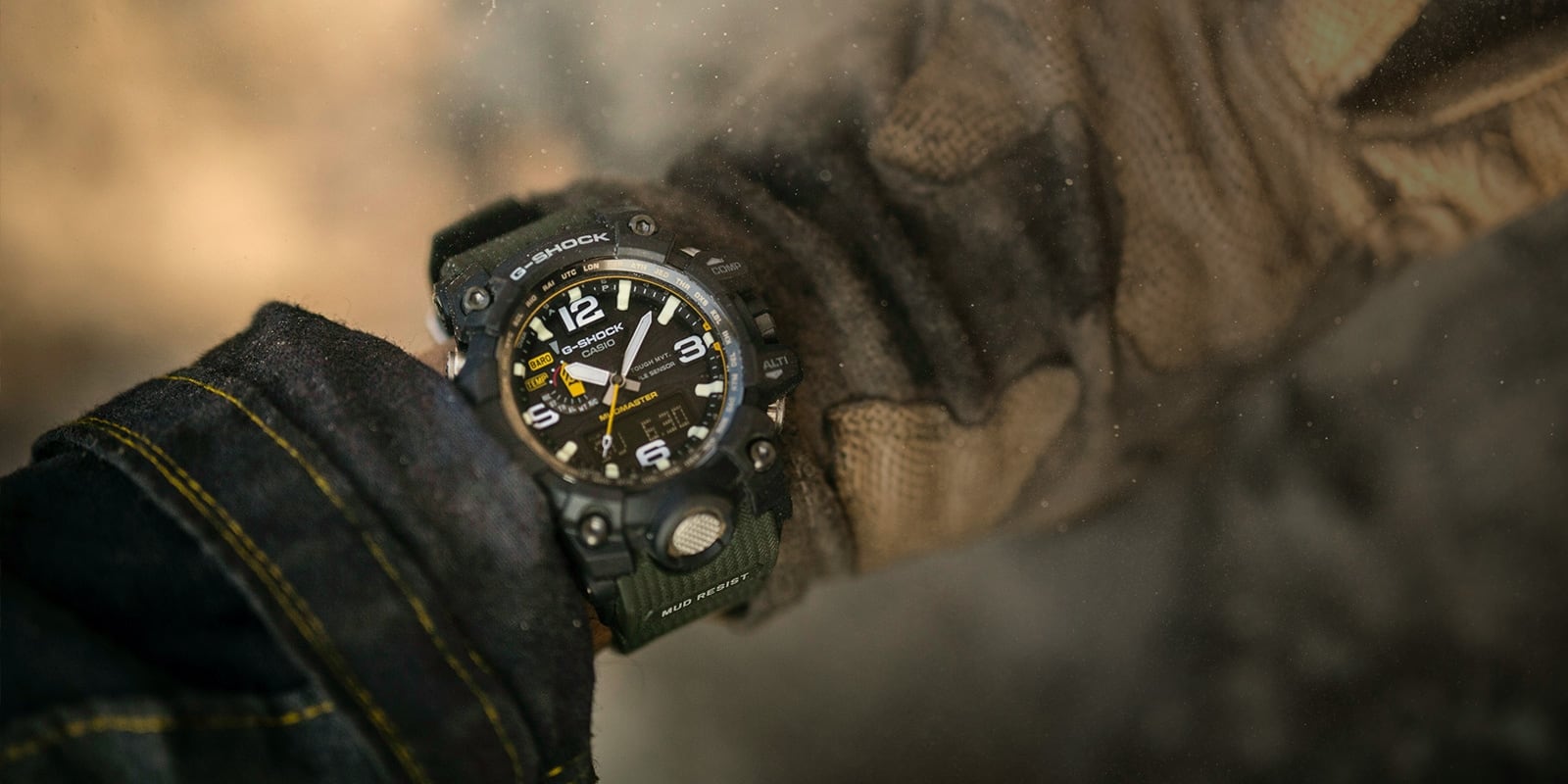 Eine Master of G Mudmaster GWG-1000-1A3 Outdoor-Uhr an einem Handgelenk zwischen Jeansjackenärmel und Arbeitshandschuhen