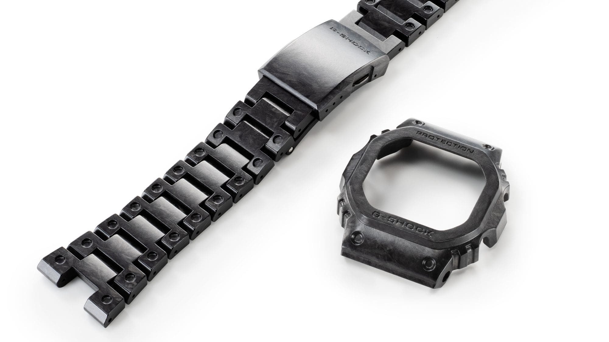 The black and grey carbon strap of the Casio G-Shock GCW-B5000UN-1 with one-touch clasp, next to it is the grey and black case
