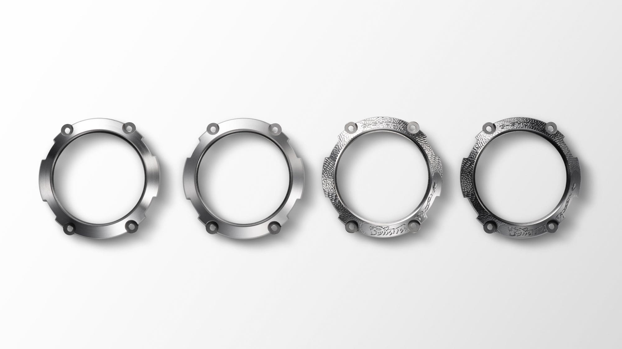 Four bezels in different stages of production - from the silver-coloured blank to the finished, dark bezel with relief pattern