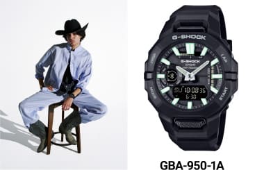 The black GBA-950 wristwatch with white-green pointers next to a person with a cowboy hat sitting on a stool wearing that watch.