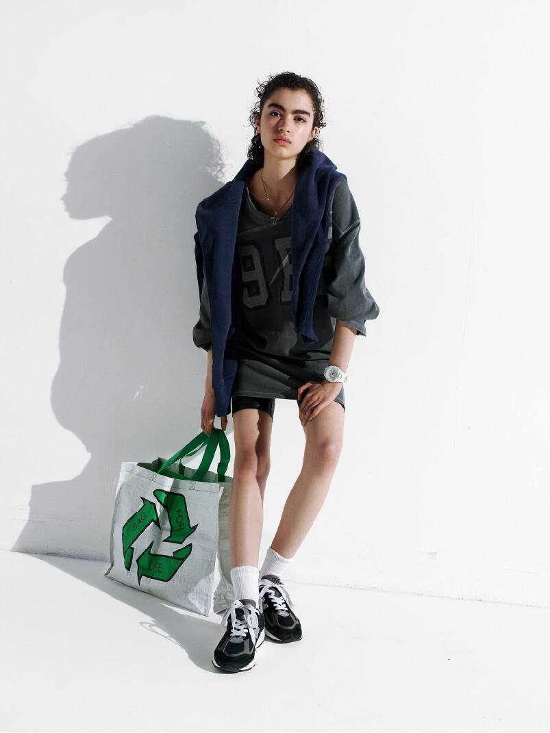Person wearing a white G-SHOCK wristwatch with an analog display holding a recycle-themed bag in a casual outfit.