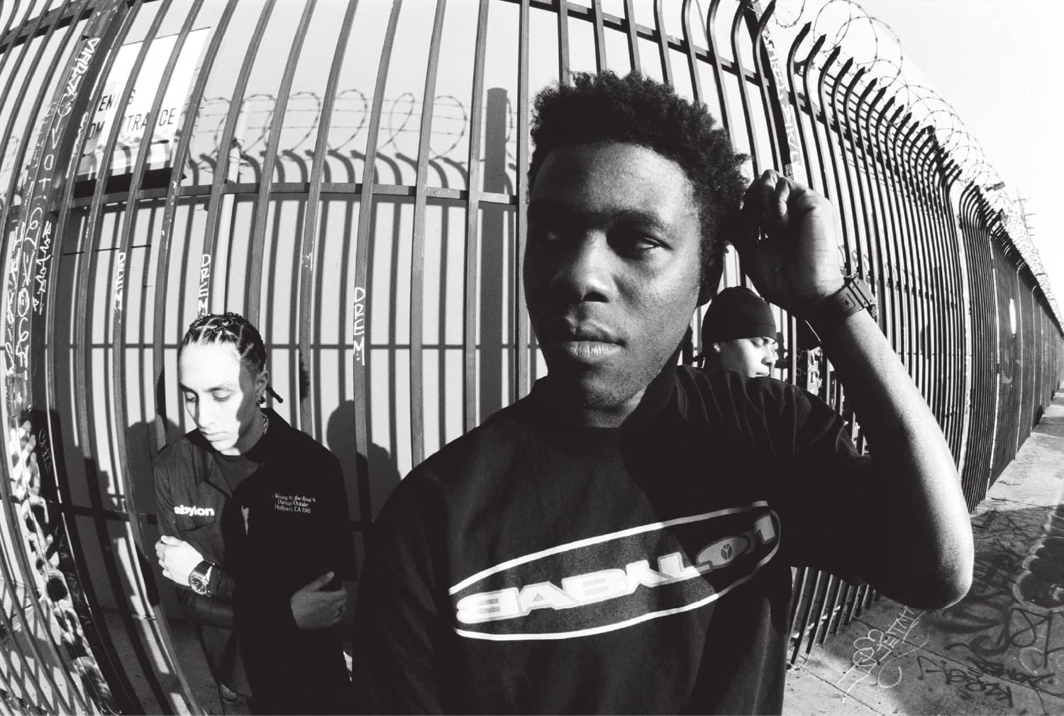 A distorted black-and-white photo of team members in front of a sturdy metal fence topped with barbed wire