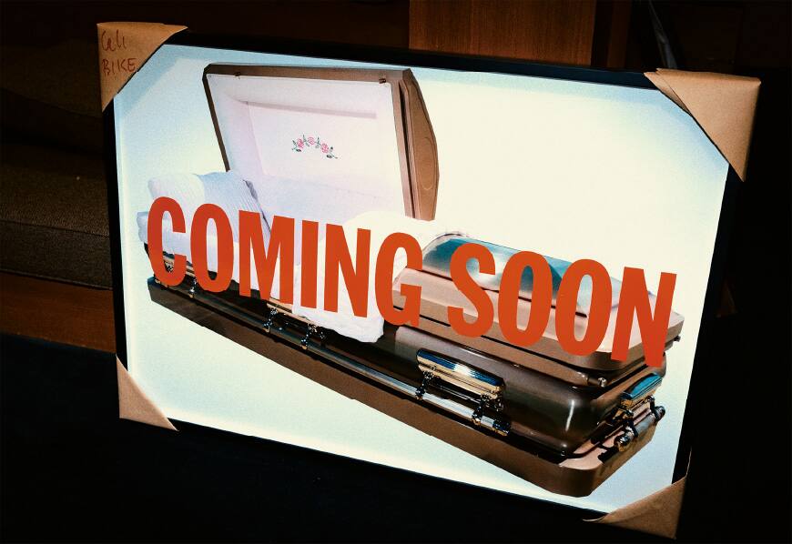 A framed picture of a coffin with the writing "coming soon" in big red letters on it