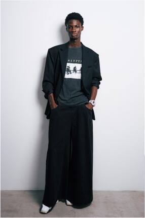 A model in dark clothes posing in front of a white wall wearing the big white GA-V01 wristwatch by G-Shock.