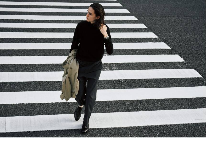 Person crossing street wearing fashion outfit with bag.