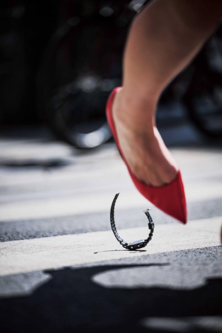 A red high heel runs over a G-Shock watch lying on a zebra crossing
