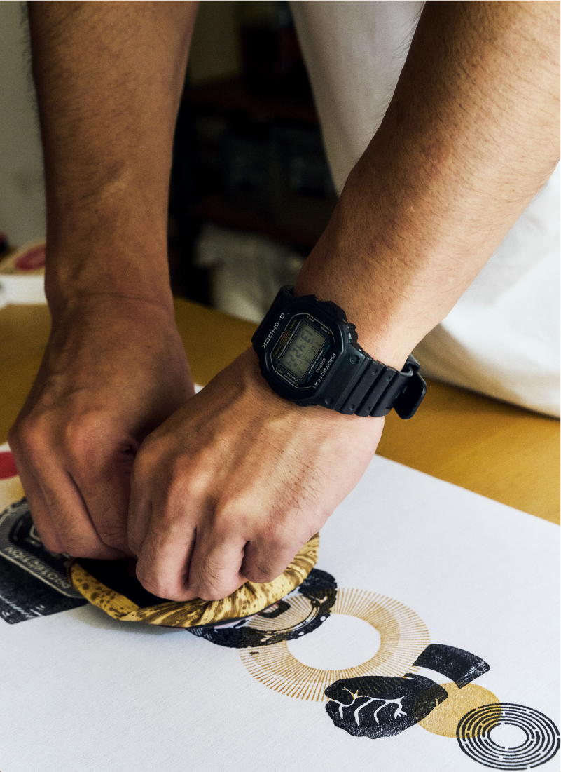 The artist T-ZUAN is working on a printmaking project and is currently stamping a graphic