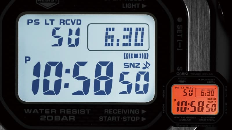 The display of a Casio G-Shock GMW-B5000 digital watch in the dark with a brightly lit dial, in front of it in small letters: the display with orange illumination