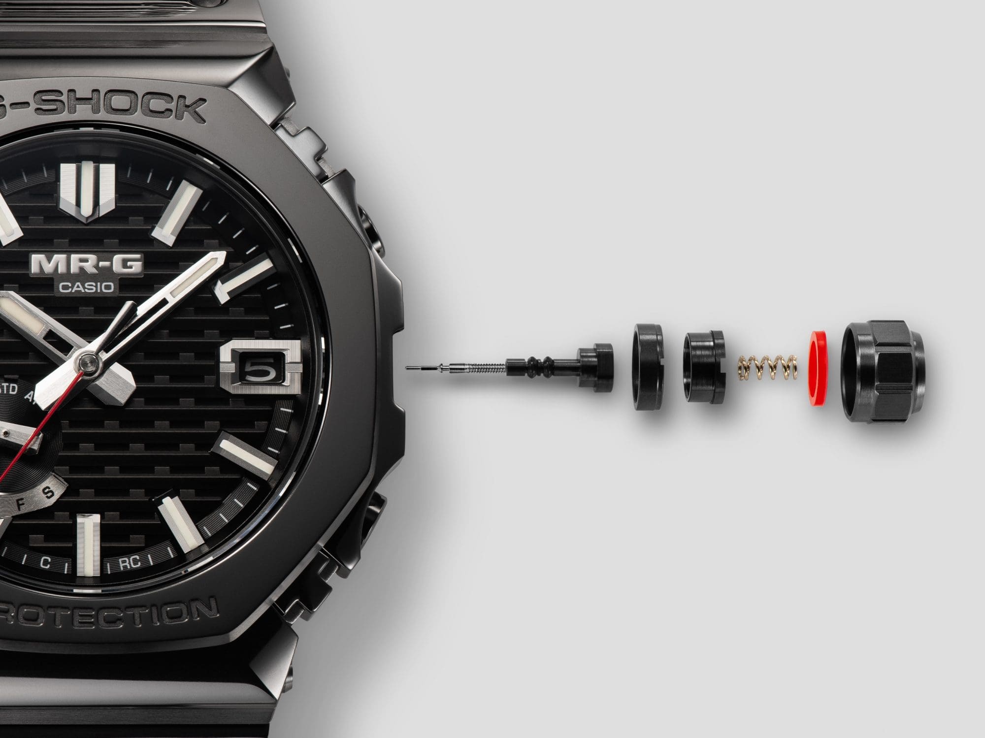 The individual components of the crown construction next to the case of the MRG-B2100B-1A wristwatch