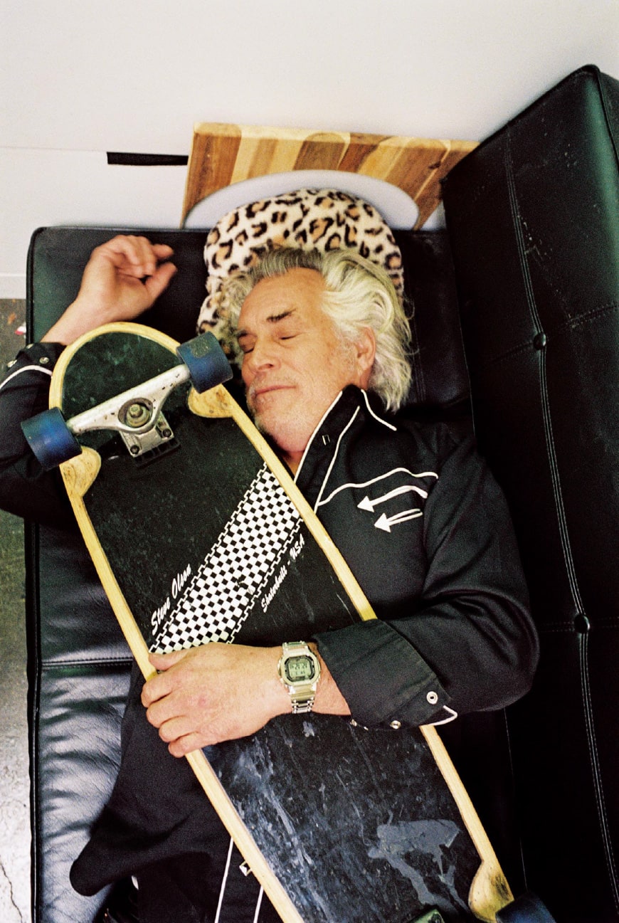A photo of Steve Olson sleeping on a sofa while holding a skateboard.