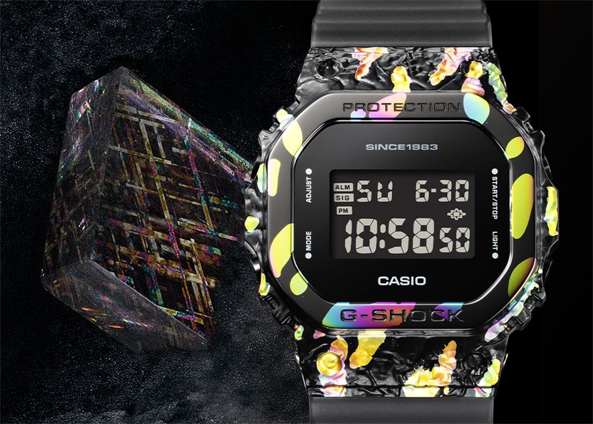 GM-5640GEM-1 El reloj aniversario GM-5640GEM-1 junto a un bloque transparente atravesado por líneas de colores del arcoíris.