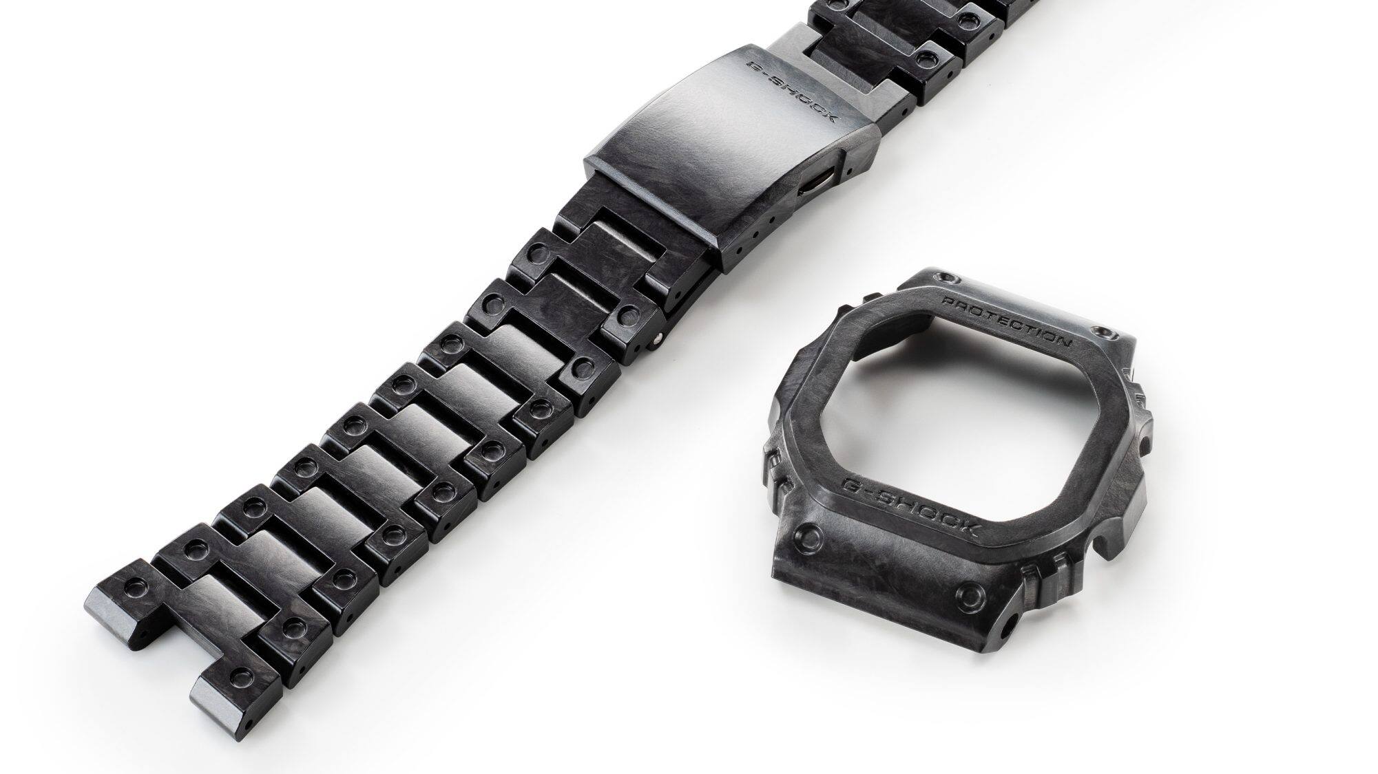 La correa de carbono negro y gris del Casio G-Shock GCW-B5000UN-1 con cierre de un solo toque, junto a la caja gris y negra.