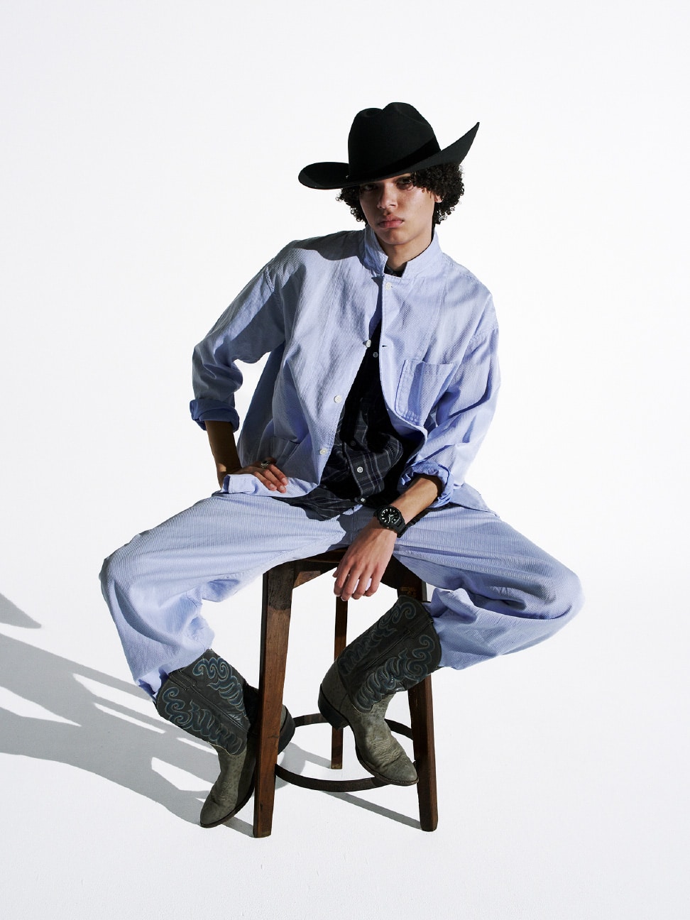 Un hombre vestido con un pantalón azul y una camisa azul claro con el G-SHOCK GBA-950 negro, sentado con sombrero de vaquero y botas.