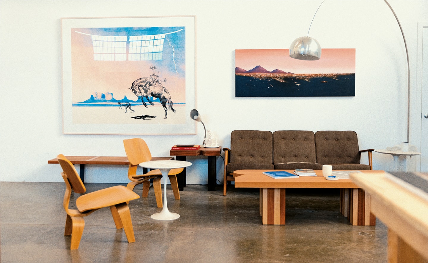 Una amplia zona de estar con una mesa de madera, un sofá marrón y sillas de madera; en las paredes cuelgan dos grandes cuadros de conocidas obras de McCormick.