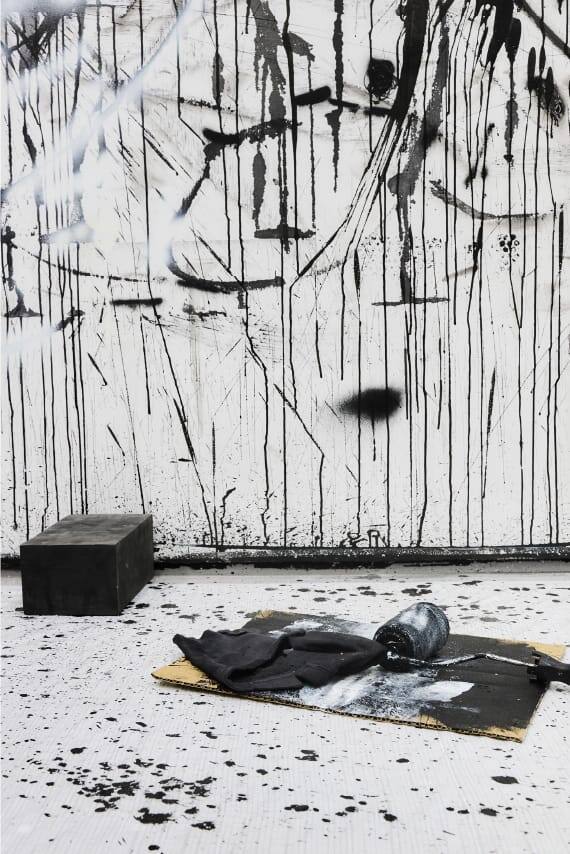 Brocha, rodillo y manchas de pintura delante de un lienzo pintado de negro.