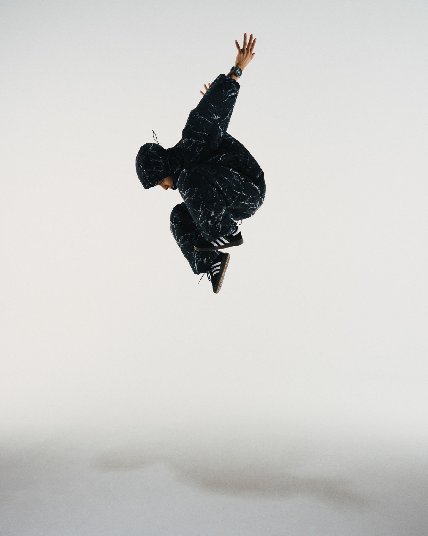 El bailarín Sei Asakura da un salto en el aire vestido de negro sobre un fondo blanco; lleva en la muñeca el reloj de pulsera G-SHOCK GA-B2100LUU-8A.