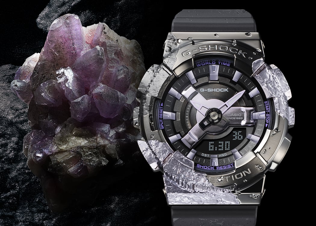 GM-S114GEM-1A2 La montre anniversaire GM-S114GEM-1A2, d'un gris foncé brillant, à côté d'un cristal de calcite violet chatoyant