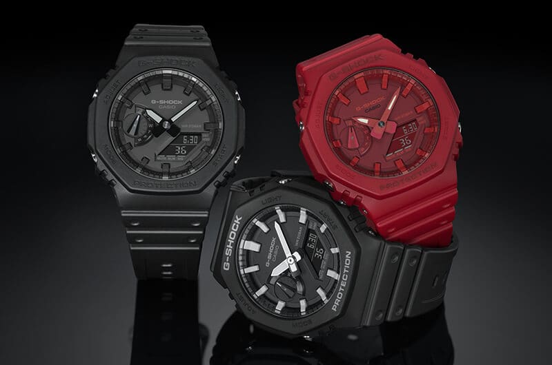 Trois montres Casio G-Shock GA-2100 devant un fond noir, deux montres sont noires, une rouge