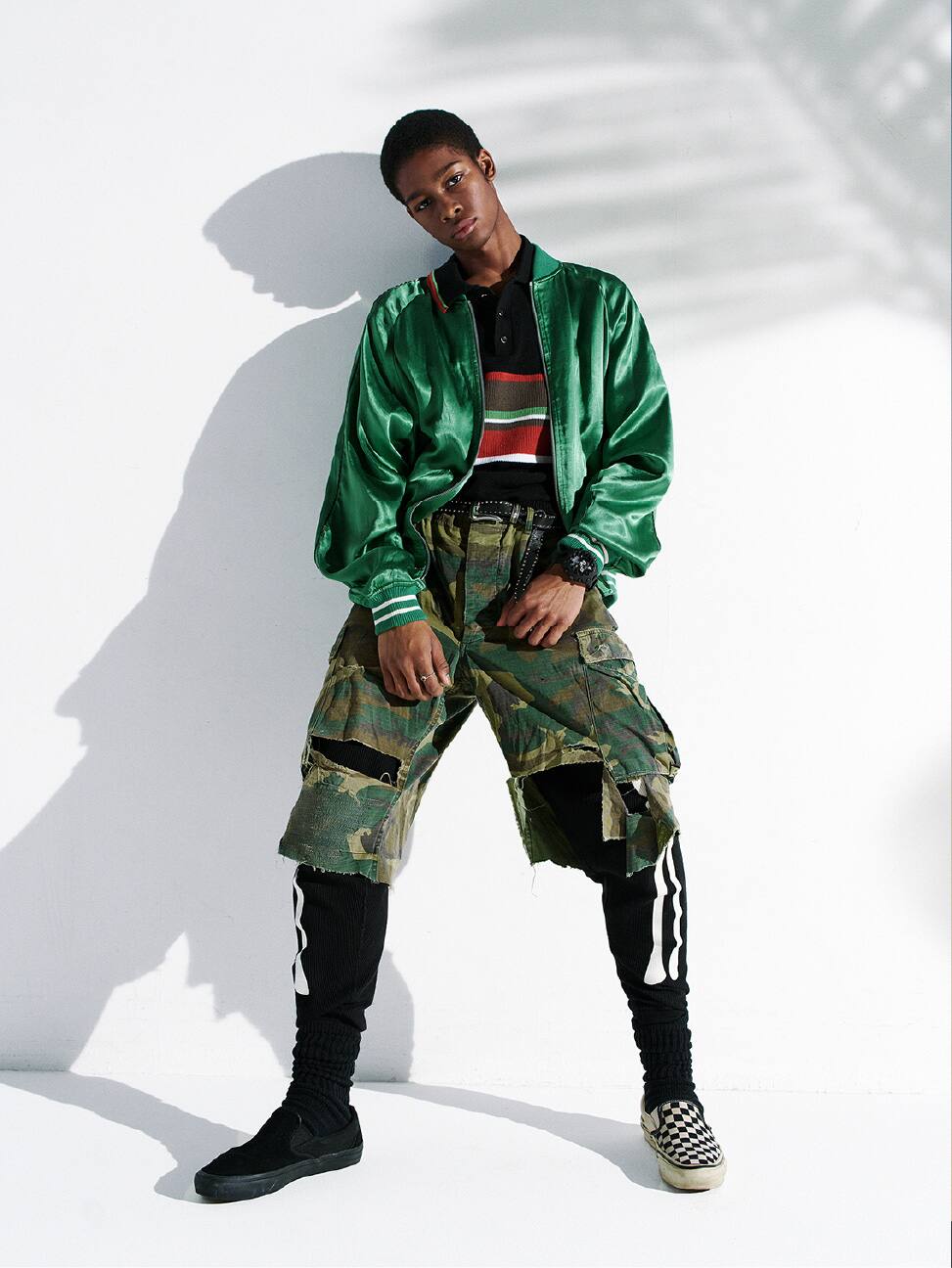 Personne portant une G-SHOCK noire, posant avec une veste en satin vert et un pantalon camouflage.