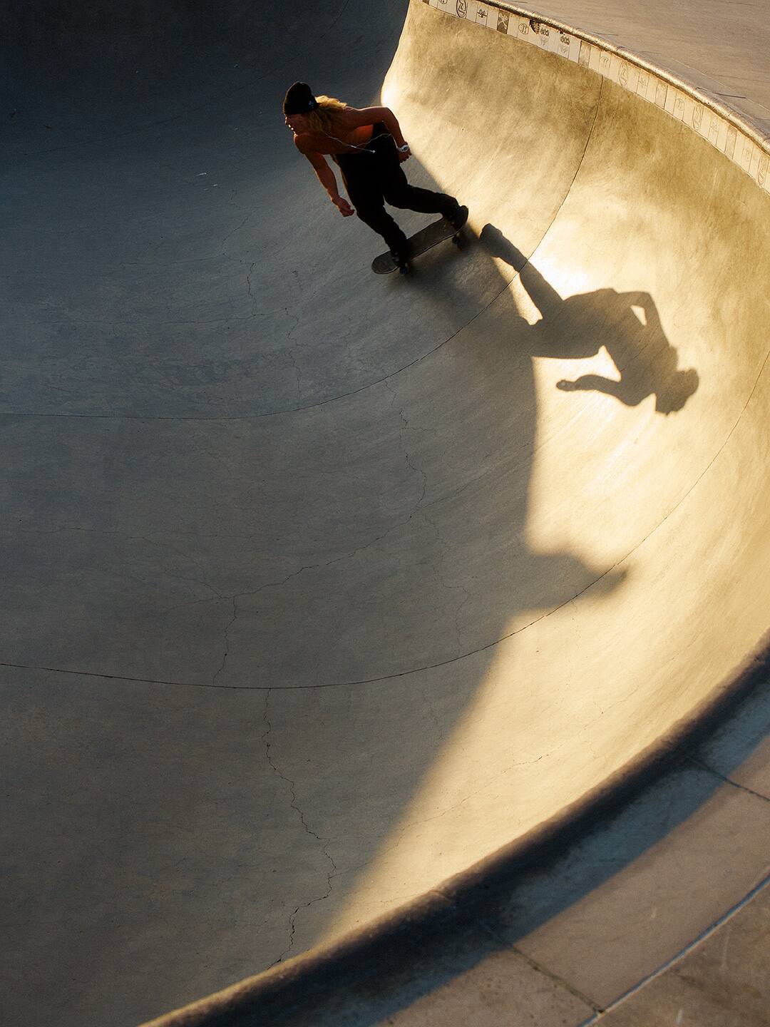 Skateboarder dans un skatepark au coucher du soleil.