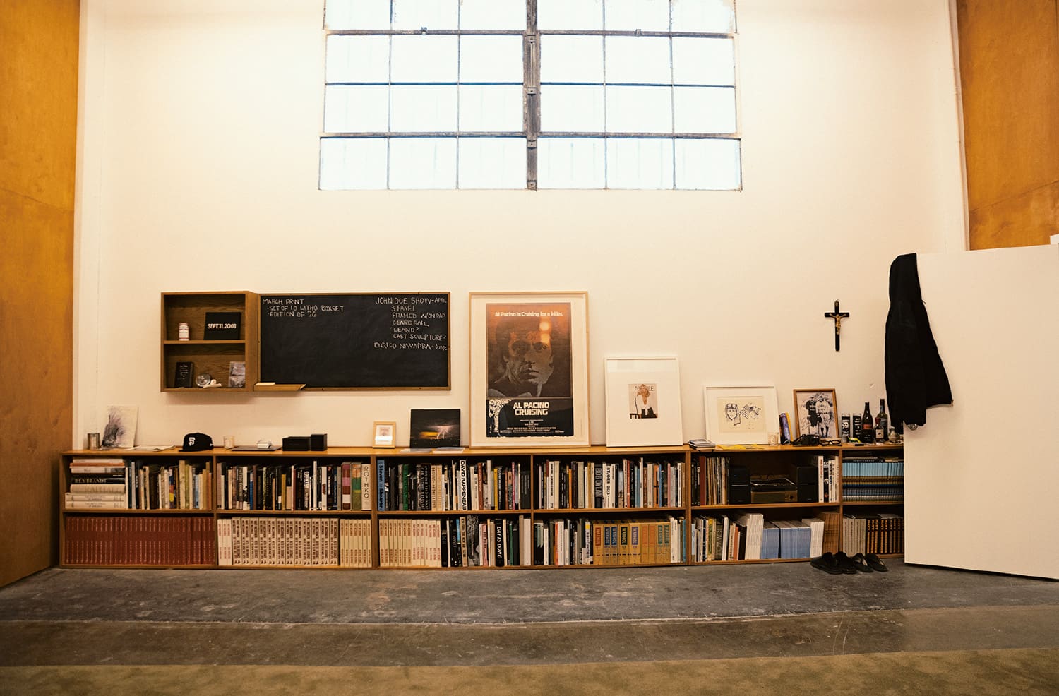 Une étagère avec des livres et des photos encadrées contre un mur blanc sous une grande fenêtre.