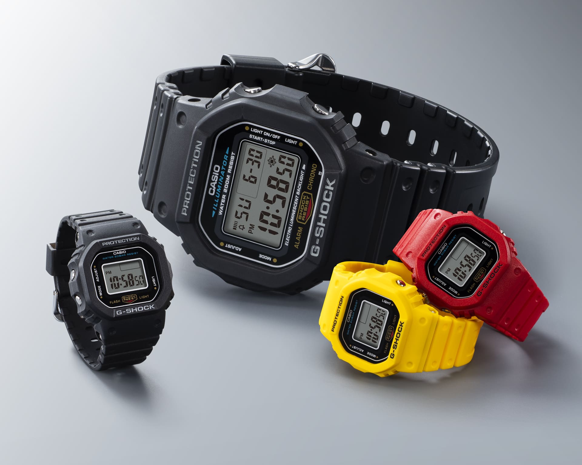Comparaison de trois montres-bagues G-SHOCK NANO en noir, jaune et rouge à côté d'une montre-bracelet G-SHOCK "conventionnelle" DW-5600.