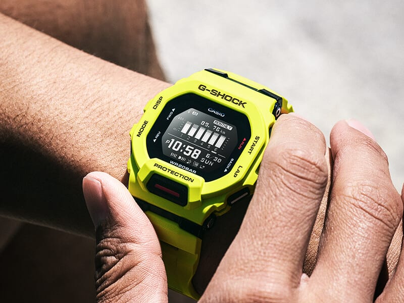 Quelqu'un porte la montre G-SQUAD GBD-200-9 Bluetooth® jaune à son poignet et appuie sur les boutons de commande latéraux.