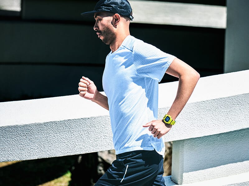 Un joggeur en short noir et t-shirt blanc porte à son bras gauche la montre de sport jaune G-SQUAD GBD-200-9