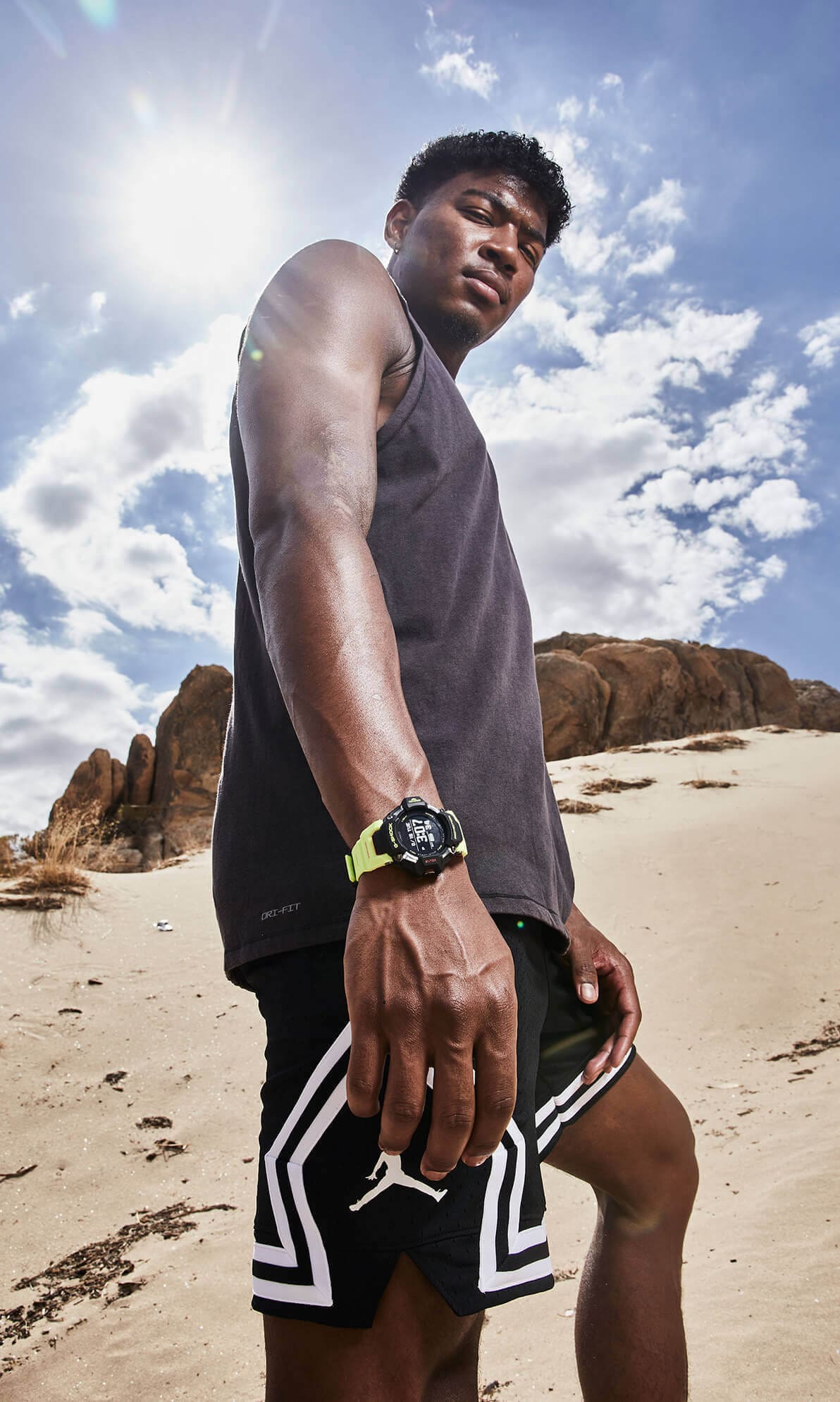 Un athlète se tient dans un paysage de sable aride et regarde la caméra d'en haut, il porte la montre Bluetooth® GBD-H2000-1A9 à son poignet.