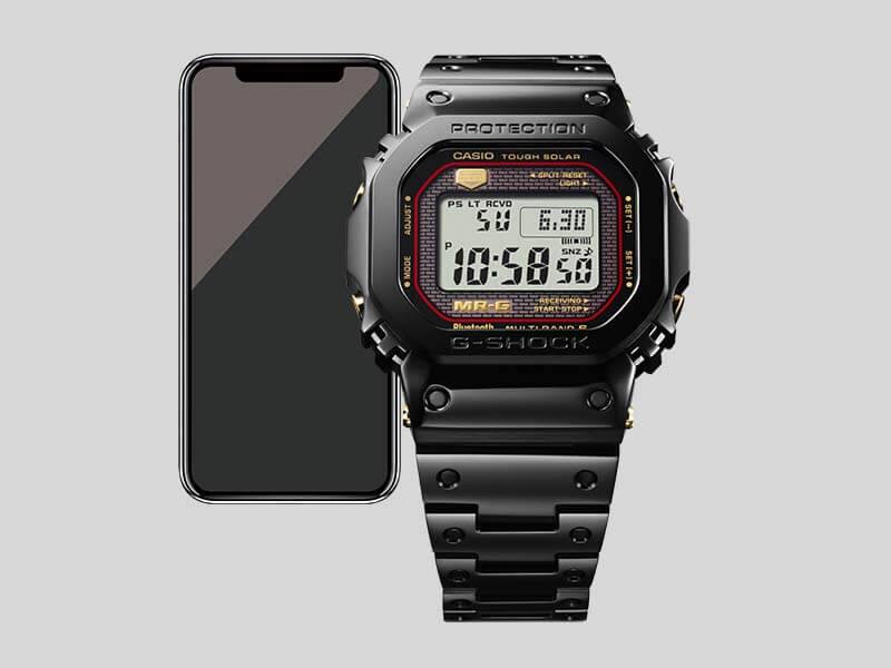 La montre noire Casio G-Shock MRG-B5000B-1 Bluetooth®, derrière : Un smartphone
