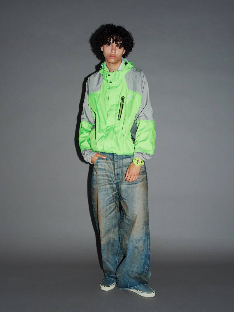 Orang yang mengenakan G-SHOCK neon dan jaket hijau, berdiri dengan pose santai.