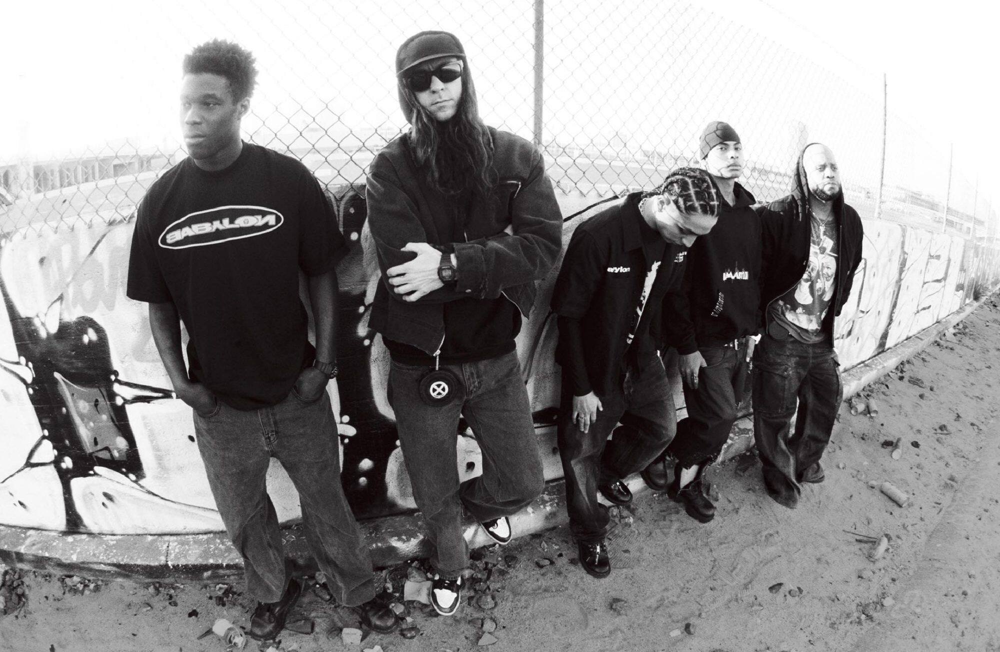 I membri di Babylon LA sono appoggiati con nonchalance a una recinzione in rete metallica.