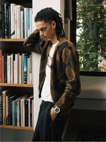 Una persona in biblioteca accanto a una libreria che indossa abiti casual e il G-Shock GM-2100M-1A con cinturino nero e lunetta ottagonale color argento.