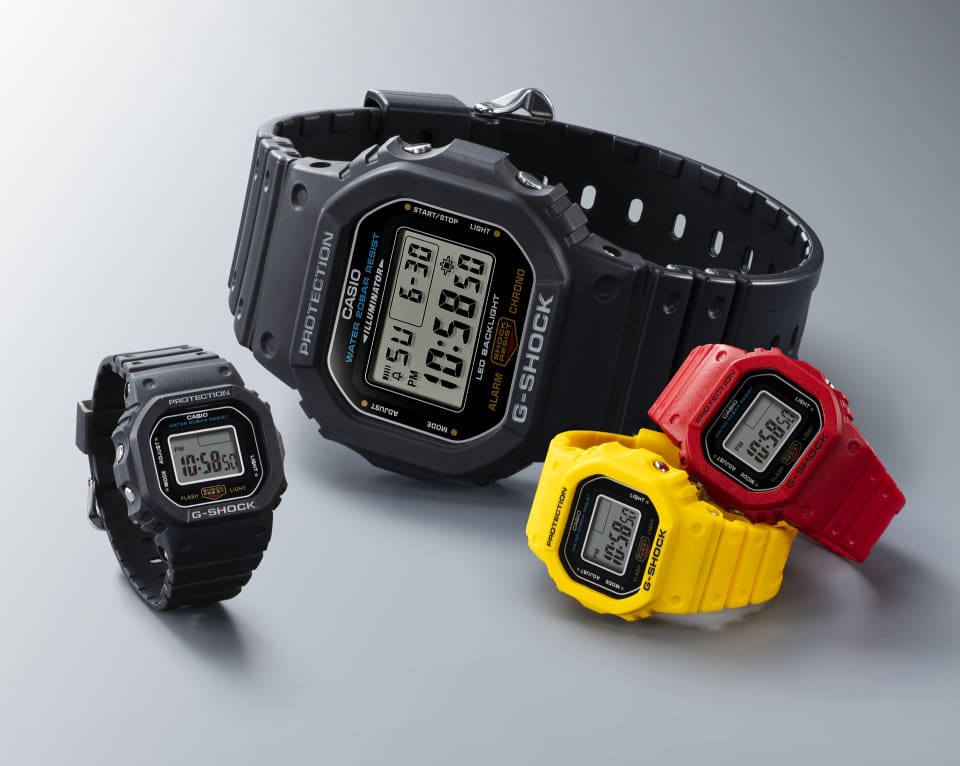 Un confronto tra tre orologi ad anello G-SHOCK NANO nei colori nero, giallo e rosso accanto a un orologio da polso G-SHOCK "convenzionale" "DW-5600".
