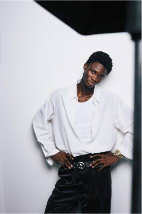 Young man wearing a metallic G-SHOCK, posing with arms resting on a chair.