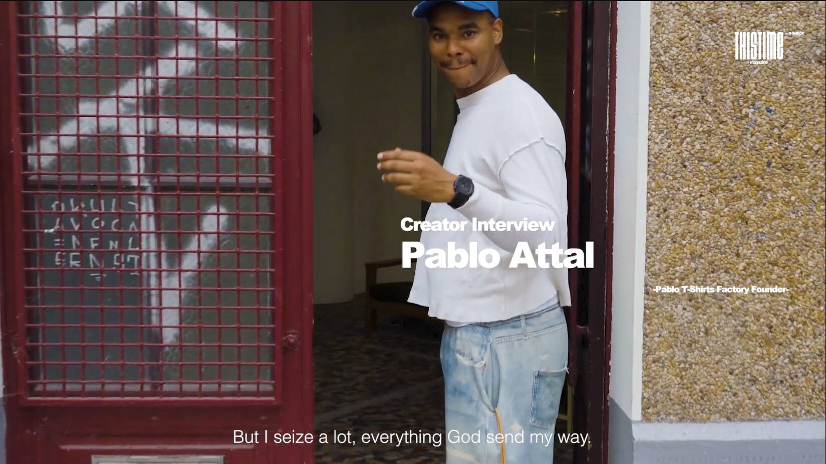 នាយកវិចិត្រករ 黒いキャップをかぶり、ドアの前で話す。