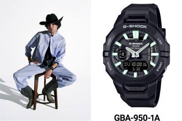 Het zwarte GBA-950 polshorloge met witgroene wijzers naast een persoon met een cowboyhoed die op een kruk zit en dat horloge draagt.