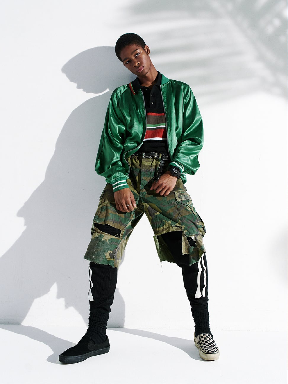 Persoon draagt een zwarte G-SHOCK, poseert in een groen satijnen jack en camo broek.