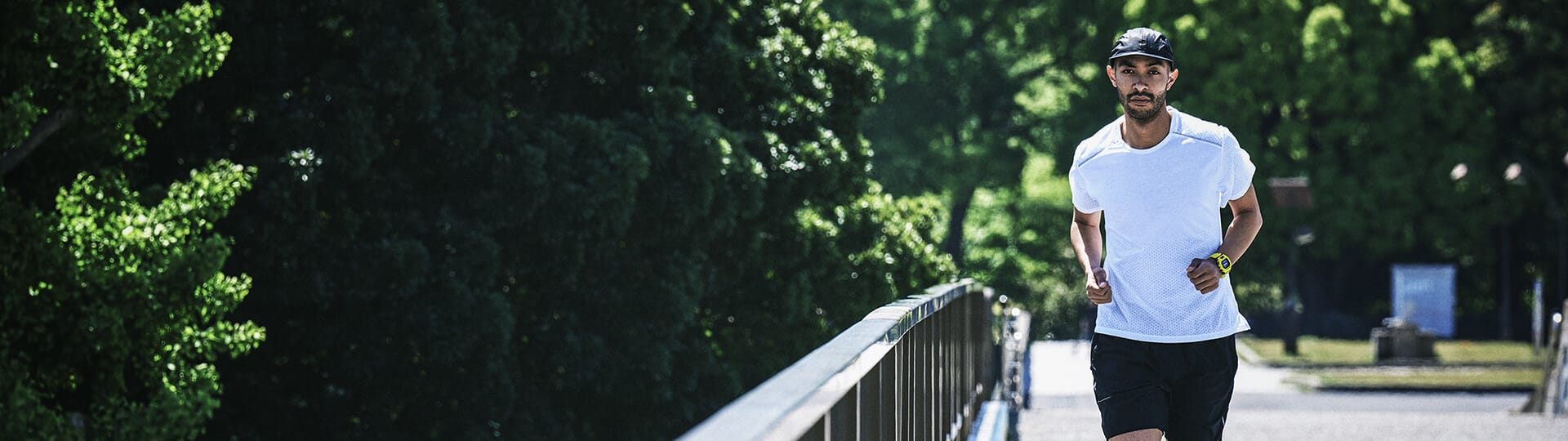 Een man in een wit T-shirt en een zwarte korte broek jogt op een brug.
