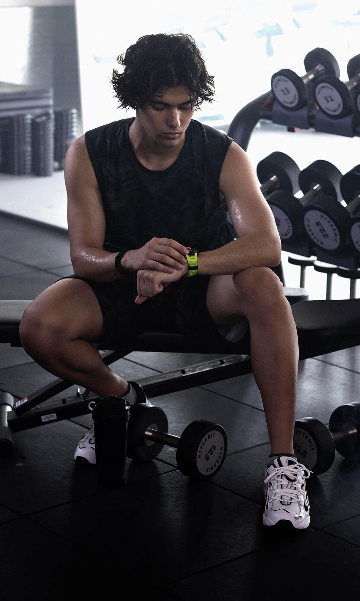 Een atleet zit op een gewichtenbank in de sportschool en kijkt naar zijn polshorloge