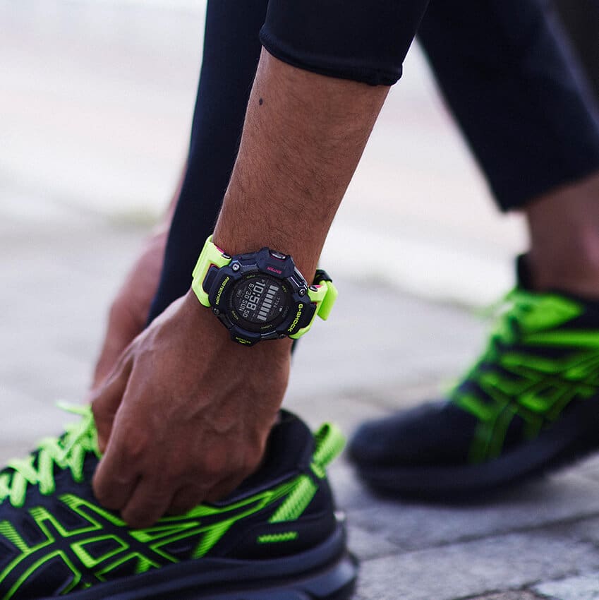 Iemand strikt de veters van zijn hardloopschoenen, met het gele GBD-H2000-1A9 hardloophorloge met zwarte kast om zijn pols
